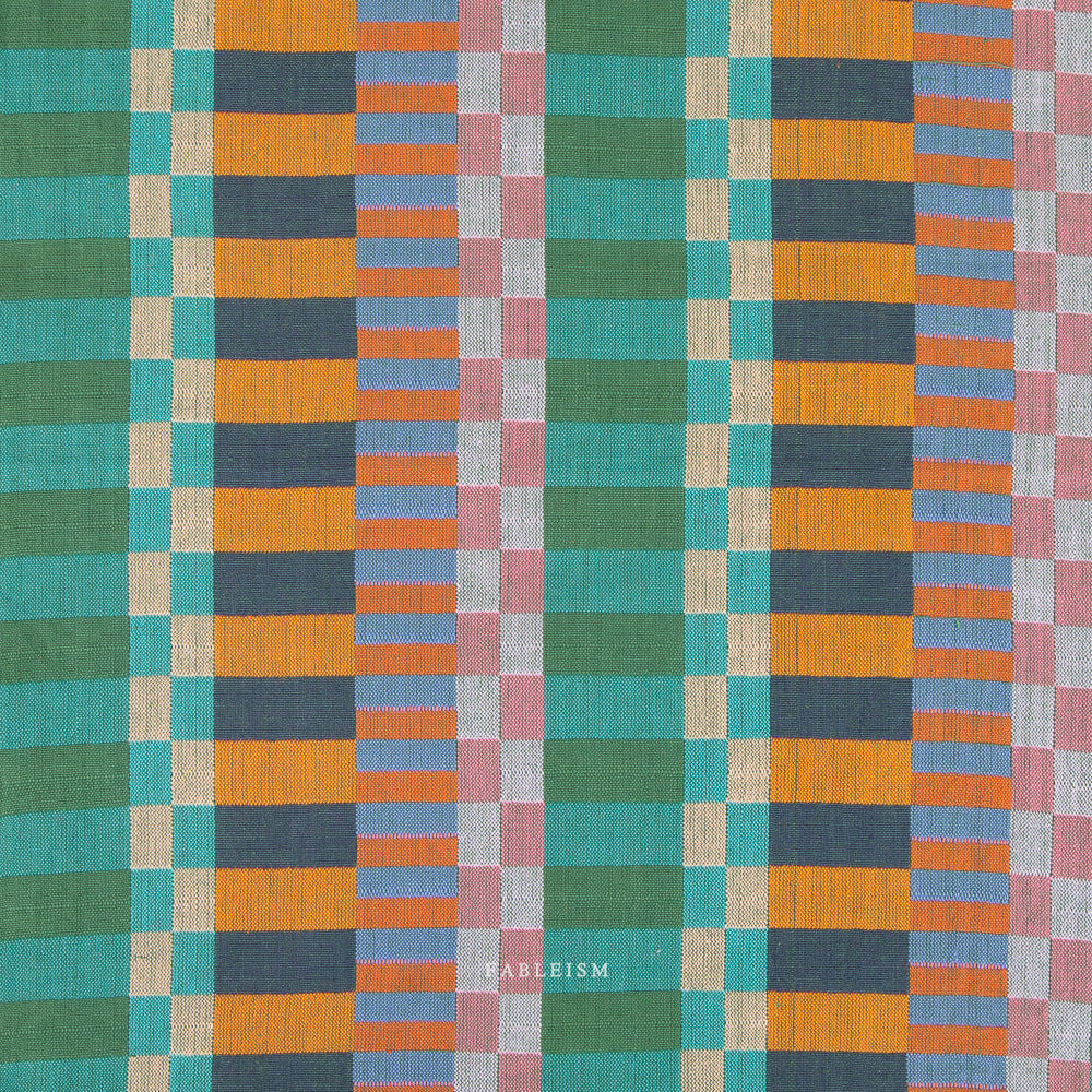 Colorful checkered fabric, greens, blues, & oranges. With the brand name, Fableism at the bottom, on a white background