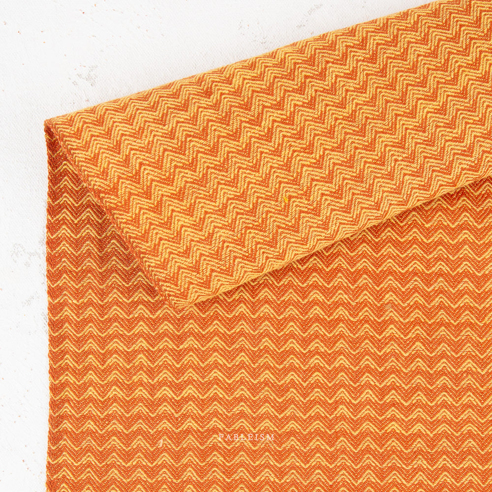 A close-up of textured fabric with a repeating orange and light orange chevron pattern, draped to show its soft texture and folds.