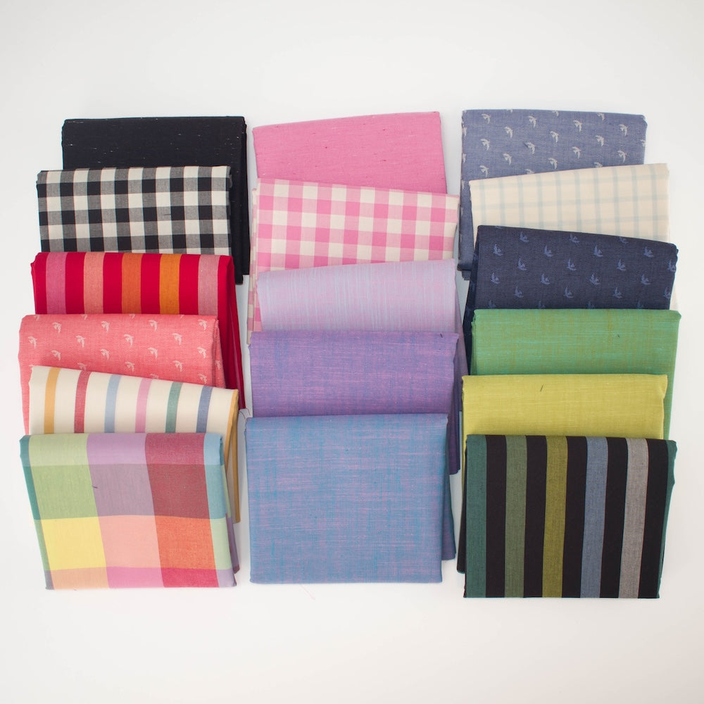 A circular arrangement of folded fabric pieces in multiple colors and patterns, including pink gingham, lavender, blue, cream plaid, green, yellow, orange stripes, black-and-white gingham, and striped fabrics, displayed on a white background.