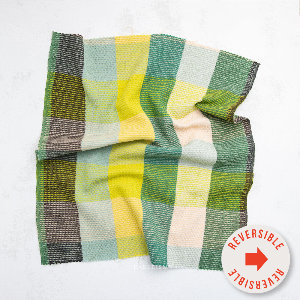 Close-up of a plaid fabric with green, yellow, and brown colors on a white background.